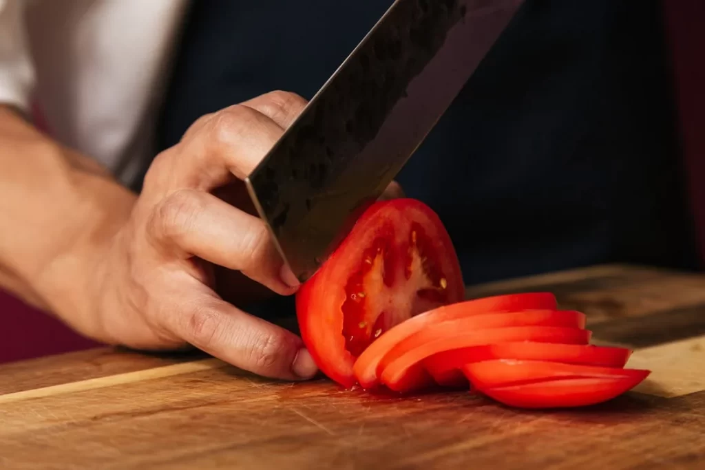 A Person using Knife while Slicing Tomatoes
